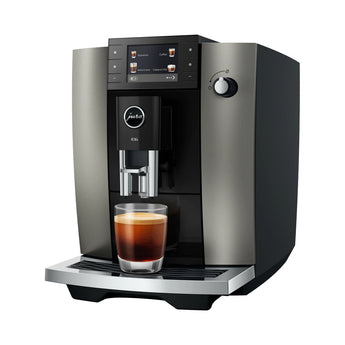 Jura E6 bean-to-cup coffee machine in Dark Inox with a glass of fresh coffee, on white