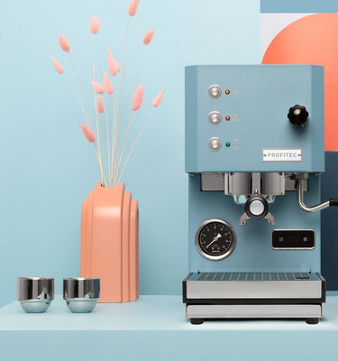 Blue Profitec Go Espresso machine on a blue platform with abstract geometric design in the background